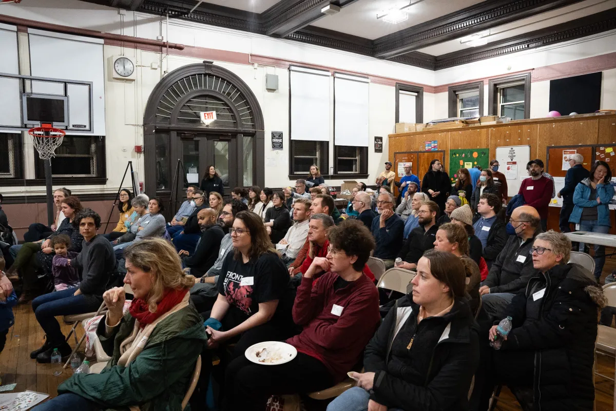 A crowded Hyde Park Avenue public meeting with residents seated and standing in a school auditorium