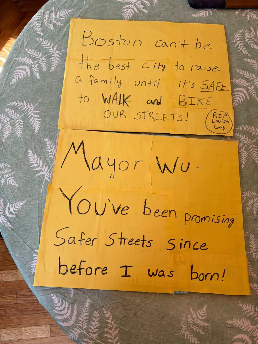 Handmade yellow signs calling on Boston and Mayor Wu to make streets safer for walking and biking